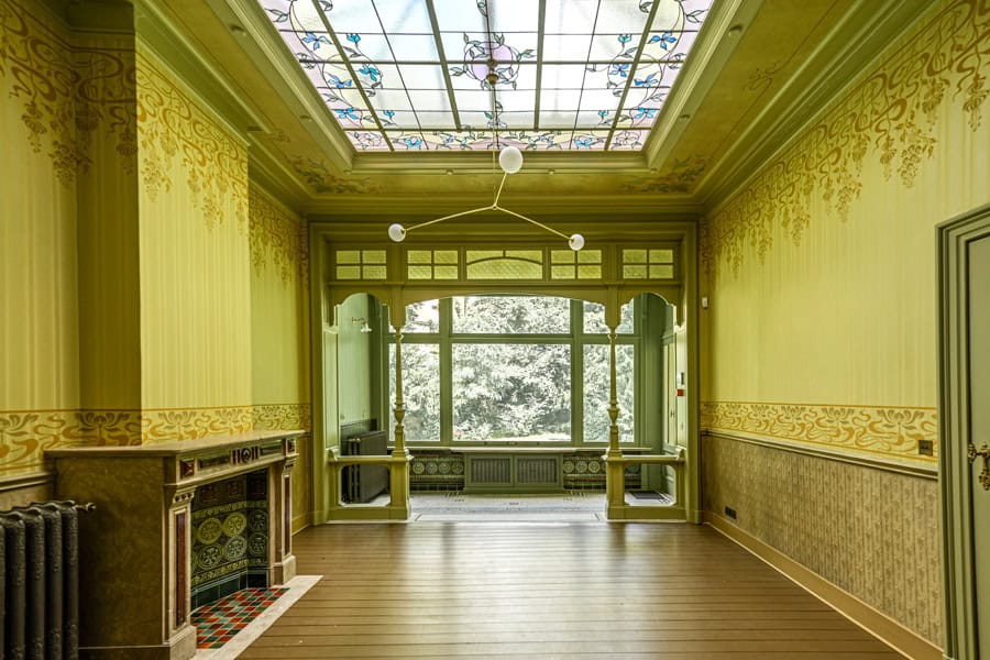 Ancien salon élégant avec vue sur la verdure, lumière tamisée et décoration raffinée.